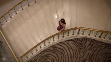 asian woman on staircase examines phone, asian woman pauses on spiral staircase to check her phone
