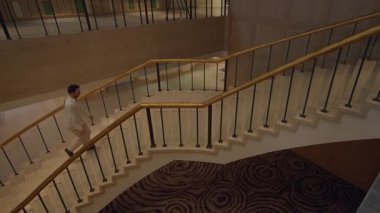 professional man walking confidently on ornate curved staircase within luxurious hotel atrium