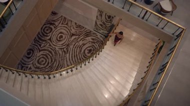 elegant hotel arrival, stylish spiral staircase with guest walking toward marble steps in luxurious