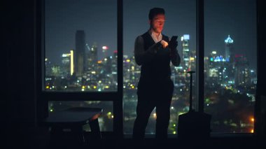 A young man dressed in a stylish suit enjoys the breathtaking city views while using his mobile phone at night