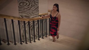 elegant woman resting, hotel guest exudes confidence on intricate staircase landing in evening dress