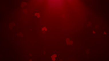 Koyu kırmızı kalpler yavaşça spot ışıklarında süzülüyor, samimi ortam sahnesinde sıcak bir parıltı.