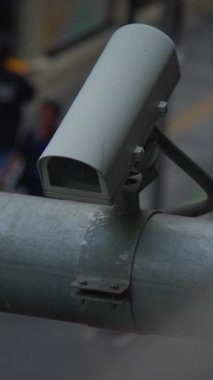 Korkuluklara yakın çekim güvenlik kamerası. Yoğun kaldırımları, mağazaları, kumlu şehir atmosferini, metali izliyoruz.