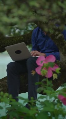 Huzurlu ve sakin bir açık hava ortamında, bir insan çiçek ve yemyeşil çiçeklerle çevrili bir dizüstü bilgisayar kullanıyor.