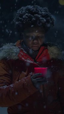 Karla kaplı bir kış gecesinde elinde kırmızı bir mum tutan bir insan, soğuk bir ortamda sıcaklık uyandırıyor..