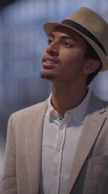 Şık ceketli ve şık şapkalı genç bir adam özgüven ve cazibe saçan düşünceli bir şekilde bakıyor.