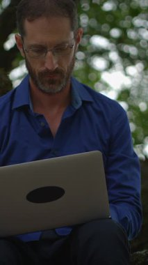 Kendini işine adamış bir profesyonel, doğal bir açık hava ortamının tadını çıkarırken dizüstü bilgisayarındaki görevlere derin bir şekilde dalmıştır.