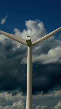 Çarpıcı bir rüzgar türbini, üzerinde dönen bulutların dramatik arka planına karşı görkemli bir şekilde yükseliyor.