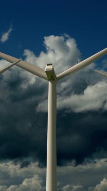 Üzerimizde dönen bulutlarla dolu kasvetli bir gökyüzüne karşı konumlanmış büyük bir rüzgar türbininin yakın görüntüsü.