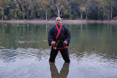 Güneşli bir günde, geleneksel üniformalı bir adam gölde sipalkido disiplini uyguluyor.