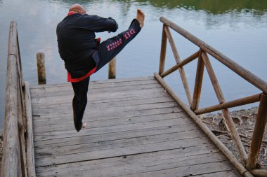 Güneşli bir günde, geleneksel üniformalı bir adam gölde sipalkido disiplini uyguluyor.