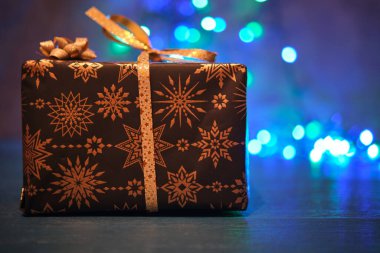 Mavi bir yüzey ve bulanık bir arka plan üzerinde siyah ve altın bir Noel hediyesi kutusu.