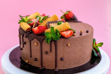 Pembe arka planda çilekle süslenmiş el yapımı çikolatalı pasta.
