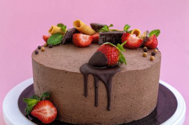 Pembe arka planda çilekle süslenmiş el yapımı çikolatalı pasta.