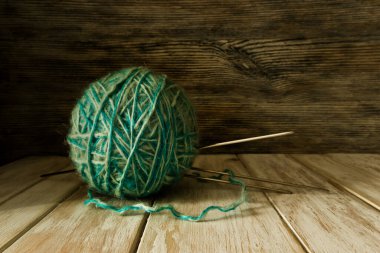 İki tonluk yün yumağı ve eski boyanmış ahşap arka planda örgü iğneleri.