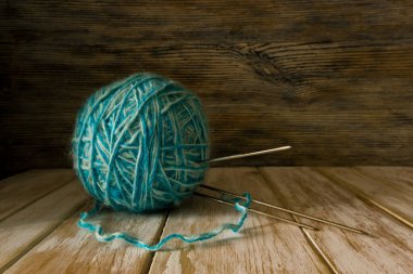 İki tonluk yün yumağı ve eski boyanmış ahşap arka planda örgü iğneleri.