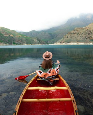 Bulutlu bir günde gölde kano yapan bir kız. Kabardino-Balkaria 'nın Bylym köyündeki Gizhgit Gölü' nün karamsar atmosferi