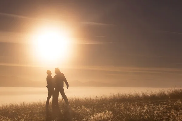 Siluet aktif pasangan cinta dengan tiang Trekking di pagi hari kabut — Stok Foto