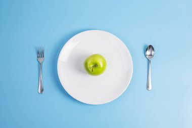 Üst manzara kaşığı ve çatal, yeşil elma beyaz seramik tabakta mavi arka planda. diyet, kilo kaybı, obezite ve gıda kontrol kavramı