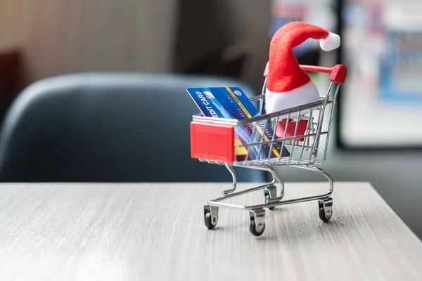 Merry Christmas with miniature Santa Clause hat, Shopping cart and credit card on table at office. Holiday, Celebration, technology, e-commerce, Black Friday, Cyber Monday and online payment concept