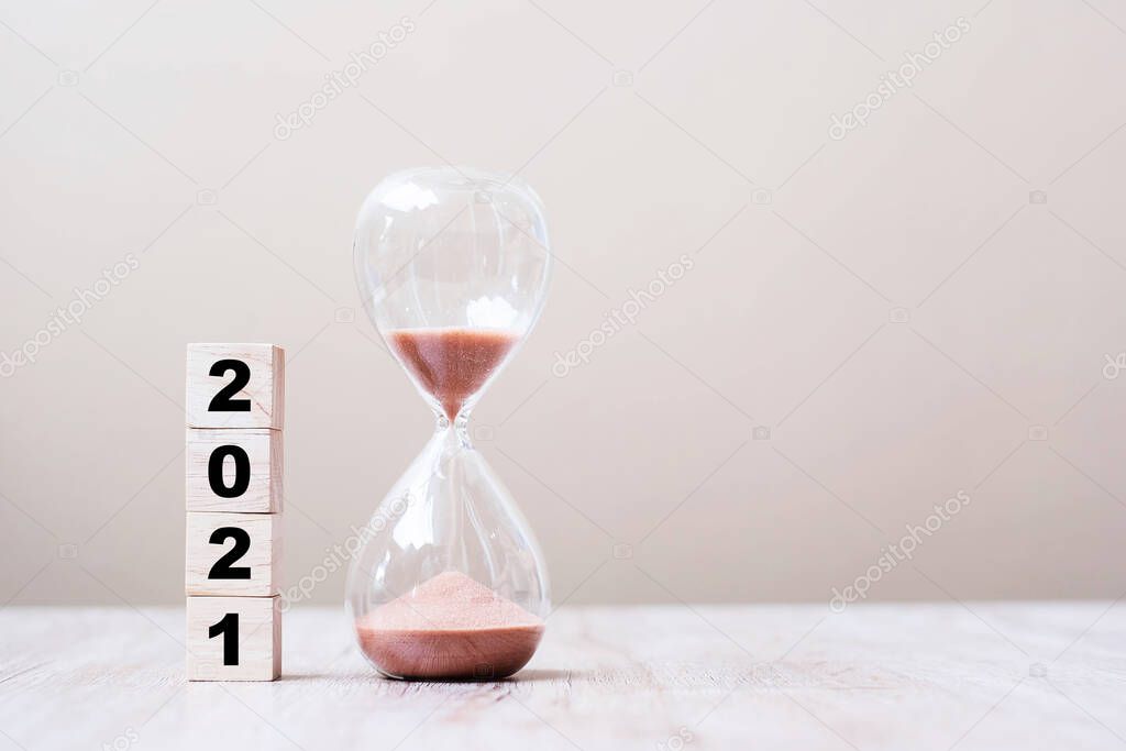 Hourglass with 2021 wooden cube blocks on table, Sand flowing through the bulb of Sandglass measuring the passing time. countdown, deadline, Happy New Year, Resolution and New Start concept