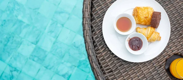 Floating Breakfast tray in swimming pool at luxury hotel or tropical resort villa, desserts; croissant, chocolate roll, pie and orange juice. Exotic summer travel, holiday and vacation concept
