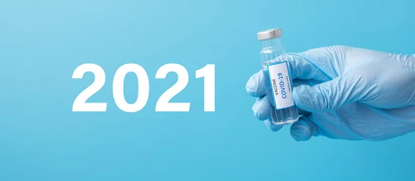 2021 happy New Year with COVID-19 Vaccine vial against Coronavirus infection in hand of doctor with Nitrile Glove in hospital laboratory. Medical, health, Vaccination and immunization concept