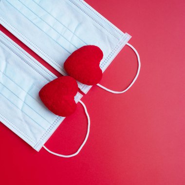 Coronavirus hastalığı enfeksiyonuna karşı kırmızı arka planda kalp şekli dekorasyonu ve tıbbi yüz maskesi. Aşk, birlikte ve Covid-19 salgını altında Sevgililer Gününüz kutlu olsun.