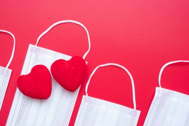 Coronavirus hastalığı enfeksiyonuna karşı kırmızı arka planda kalp şekli dekorasyonu ve tıbbi yüz maskesi. Aşk, birlikte ve Covid-19 salgını altında Sevgililer Gününüz kutlu olsun.