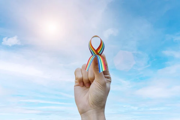 hand showing LGBTQ Rainbow ribbon against sky background in the morning. Support Lesbian, Gay, Bisexual, Transgender, Queer community and Rights concept