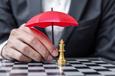 İş adamı elinde kırmızı Şemsiye ile Satranç Kralı figürünü tutuyor. İş, Risk Yönetimi, Çözüm, Ekonomik gerileme, Sigorta, Strateji ve Müdahale Kavramları