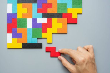 Geometrik şekil bloğunu renkli ahşap yapboz parçalarıyla birleştiren el. Mantıklı düşünme, iş mantığı, Bilmece, karar, çözümler, rasyonel, misyon, başarı, hedefler ve strateji kavramları