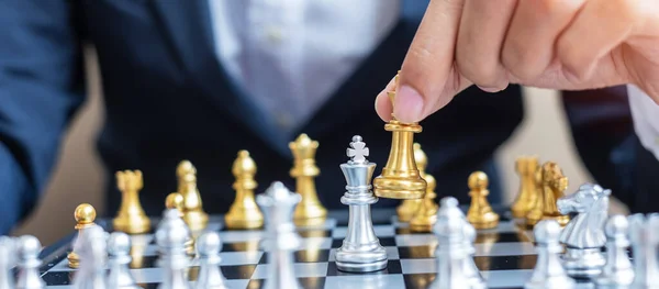 businessman hand moving gold Chess King figure and Checkmate opponent during chessboard competition. Strategy, Success, management, business planning, disruption and leadership concept