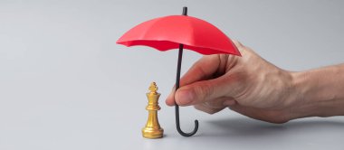 İş adamı elinde kırmızı Şemsiye ile Satranç Kralı figürünü tutuyor. İş, Risk Yönetimi, Çözüm, Ekonomik gerileme, Sigorta, Strateji ve Müdahale Kavramları