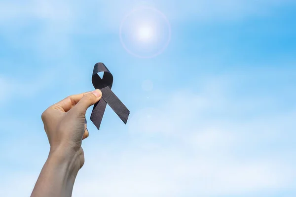 Melanoma and skin cancer, Vaccine injury awareness month and rest in peace concepts. man holding black Ribbon on sky background