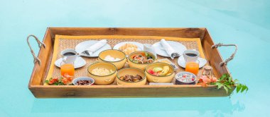 Lüks otellerde ya da tropik tatil köylerinde yüzen kahvaltı tepsileri, meyveler, kruvasan, kahve ve portakal suyu. Egzotik yaz, dinlenme, tropikal seyahat ve tatil konsepti
