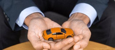 İş adamı elinde turuncu araba oyuncağı tutuyor. Finansal, para, yeniden finansman ve araba sigortası kavramı