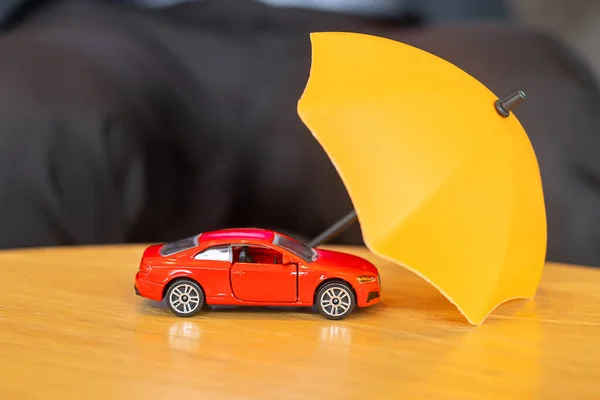 Yellow umbrella cover or protection red car toy on table. Financial, money, refinance and Car insurance concept