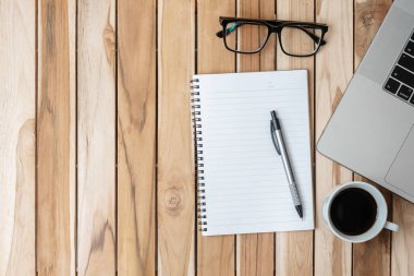 Üst kattaki ofis masasında kalem, bilgisayar dizüstü bilgisayar, boş defter, tahta arka planda saksı ve kahve fincanı. metin kavramı için kopyalama alanı olan çalışma alanı veya ev ofisi