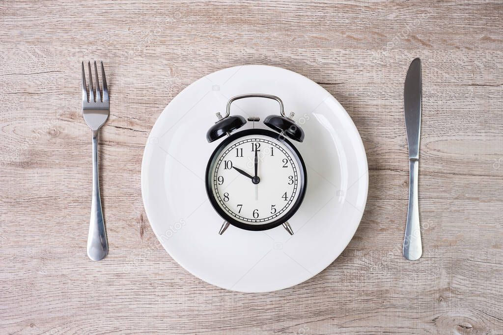 knife and fork with alarm clock on white plate on tablecloth background. Intermittent fasting, Ketogenic dieting, weight loss, meal plan and healthy food concept