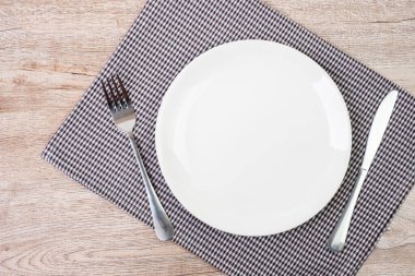 Masa arkasında çatal ve bıçak olan boş beyaz seramik tabağı. yemek ve mutfak eşyaları konsepti