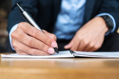 Ofiste ya da kafede deftere bir şeyler yazan takım elbiseli bir iş adamı. Kağıt raporunda imzalı kalem tutan bir adam. iş kavramları