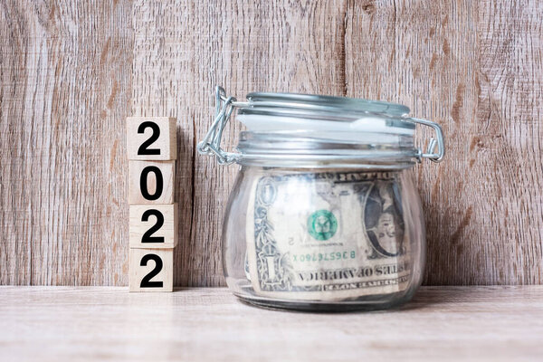 2022 Happy New Year with US dollar money glass American on wood table background. business, investment, retirement planning, finance, Saving and New Year Resolution concepts