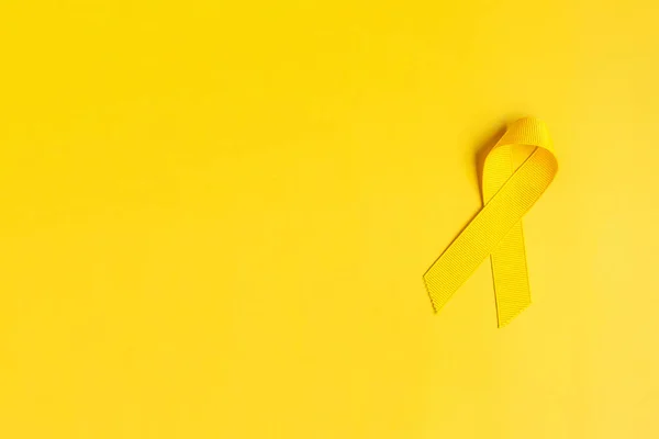 Yellow Ribbon on yellow background for supporting people living and illness. July Sarcoma cancer, Suicide prevention day, Childhood Cancer Awareness month concept