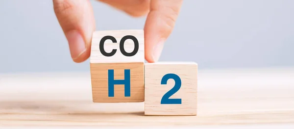 hand flipping wooden cube blocks with CO2 (Carbon dioxide), change to H2 (Hydrogen) text on table background. Free Carbon, alternative energy and global climate change concepts