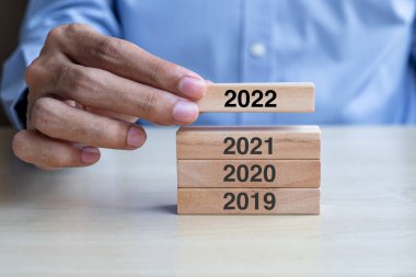 İş adamı, masa arkasında 2022 ahşap yapı taşlarını çekiyor. İş planlaması, Risk Yönetimi, Çözüm, Strateji, Çözüm, Hedef, Yeni Yıl Yeni Sen ve Mutlu Noeller kavramları