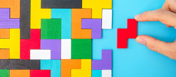 Рука, соединяющая красочные кусочки деревянной головоломки на синем фоне, геометрический блок формы. Конфеты логического мышления, Conundrum, решения, рациональные, стратегии, всемирный логический день и Образование