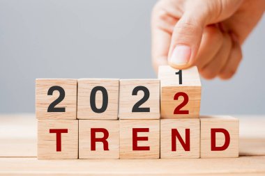 Businessman hand holding wooden cube and flip over block 2021 to 2022 TREND on table background. Resolution, plan, review, change, goal and New Year holiday concepts