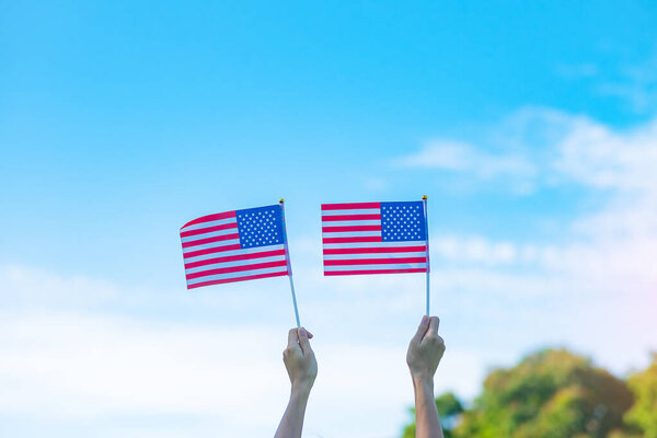 hand holding United States of America flag on blue sky background. USA holiday of Veterans, Memorial, Independence ( Fourth of July) and Labor Day concept