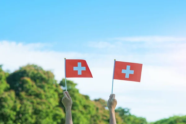 青い空を背景にスイス国旗を掲げている手 スイス国民の日と幸せなお祝いの概念 — ストック写真